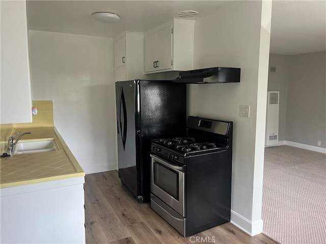 kitchen with stainless steel gas stove, tile counters, under cabinet range hood, white cabinetry, and a sink