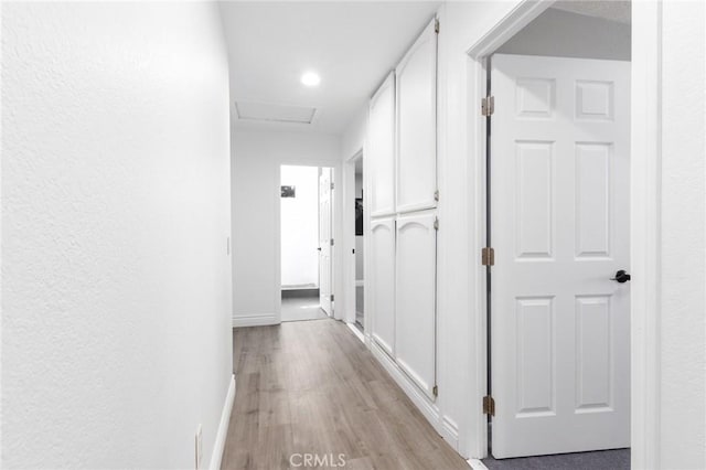 hallway featuring light wood finished floors, attic access, and baseboards