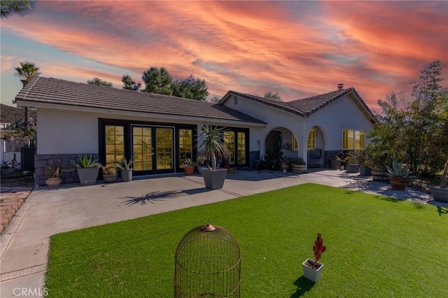 back of property featuring stone siding, stucco siding, a yard, and a patio