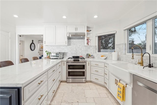 kitchen featuring stone tile floors, appliances with stainless steel finishes, a sink, a peninsula, and under cabinet range hood