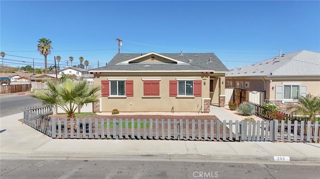 bungalow-style home with a shingled roof, a fenced front yard, and stucco siding