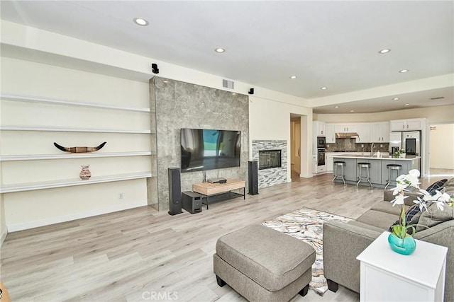 living area featuring light wood-type flooring, visible vents, a glass covered fireplace, and recessed lighting