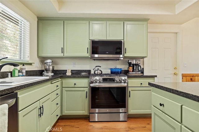 kitchen featuring stainless steel appliances, green cabinetry, a sink, and light wood finished floors