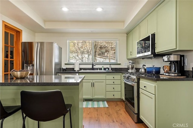 kitchen featuring a tray ceiling, light wood finished floors, stainless steel appliances, a sink, and green cabinetry