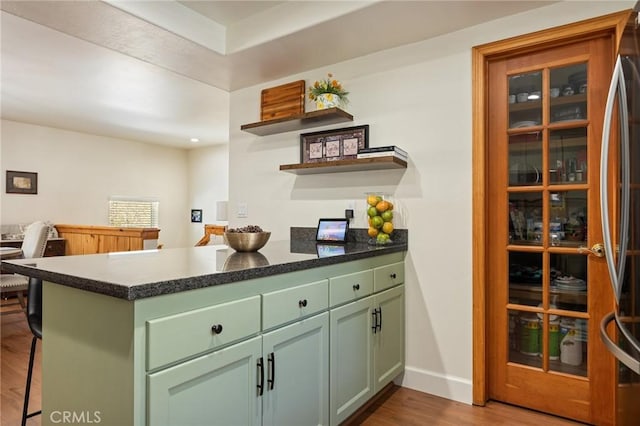 kitchen with a peninsula, green cabinets, freestanding refrigerator, dark wood-style floors, and open shelves