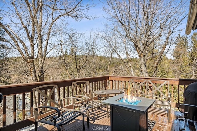 wooden terrace featuring a forest view and an outdoor fire pit