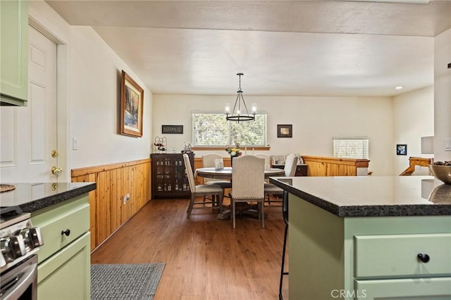 kitchen with stainless steel range with gas cooktop, a wainscoted wall, a chandelier, light wood-type flooring, and green cabinetry