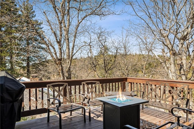 deck featuring an outdoor fire pit, a grill, and a wooded view