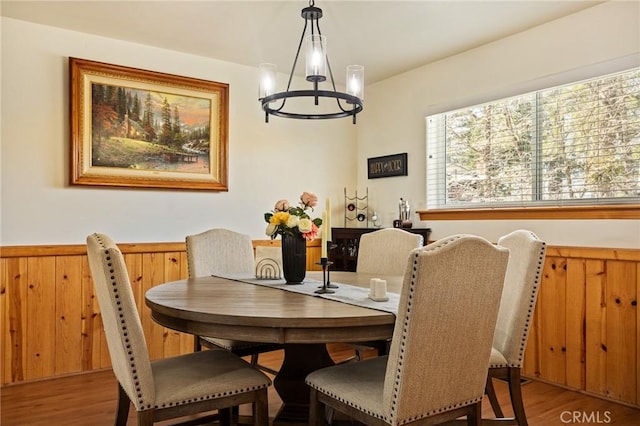 dining area featuring wooden walls, wainscoting, wood finished floors, and an inviting chandelier