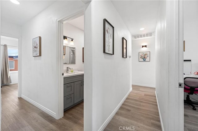 corridor with baseboards, a sink, visible vents, and light wood-style floors