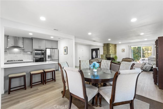 dining room with light wood-type flooring, visible vents, a stone fireplace, and recessed lighting