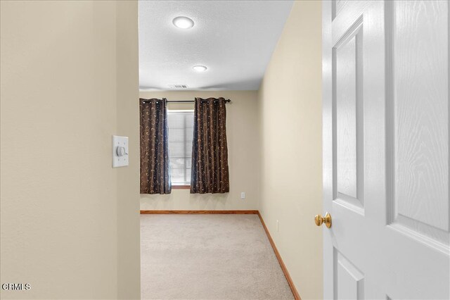 carpeted empty room featuring a textured ceiling and baseboards