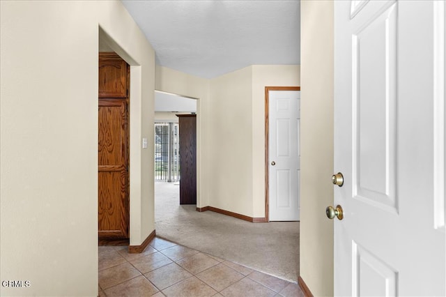 hall with light tile patterned floors, baseboards, and light colored carpet