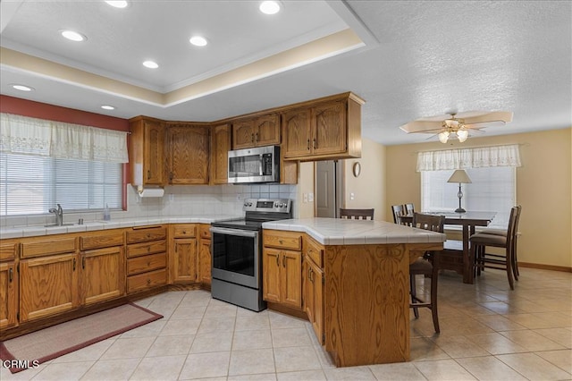 kitchen featuring light tile patterned floors, a raised ceiling, decorative backsplash, appliances with stainless steel finishes, and a peninsula