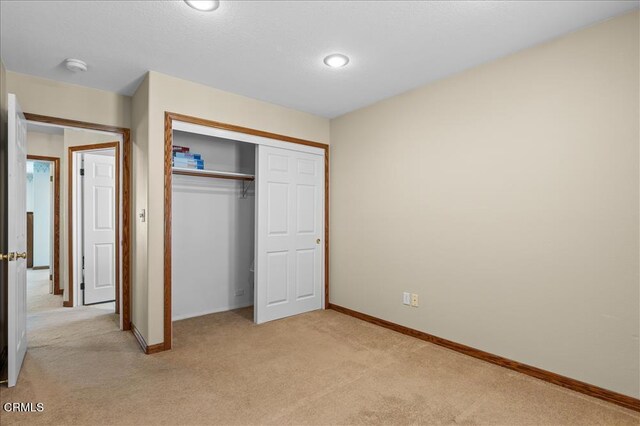 unfurnished bedroom with a closet, light colored carpet, and baseboards