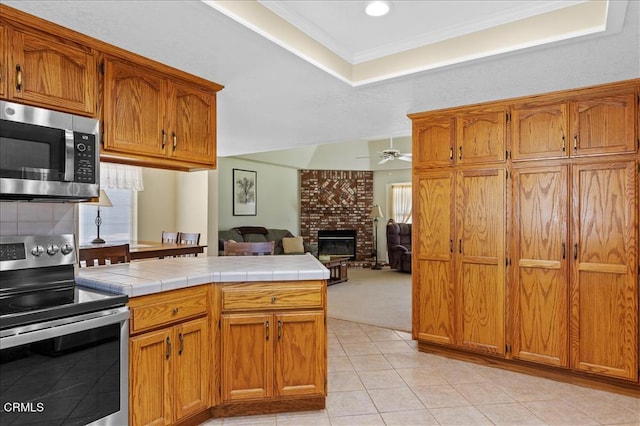 kitchen featuring tile countertops, appliances with stainless steel finishes, a ceiling fan, and brown cabinets