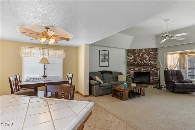 living area featuring a fireplace, light carpet, ceiling fan, a textured ceiling, and light tile patterned flooring