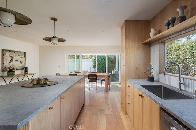 kitchen with a sink, light brown cabinetry, light wood-type flooring, open shelves, and stainless steel dishwasher