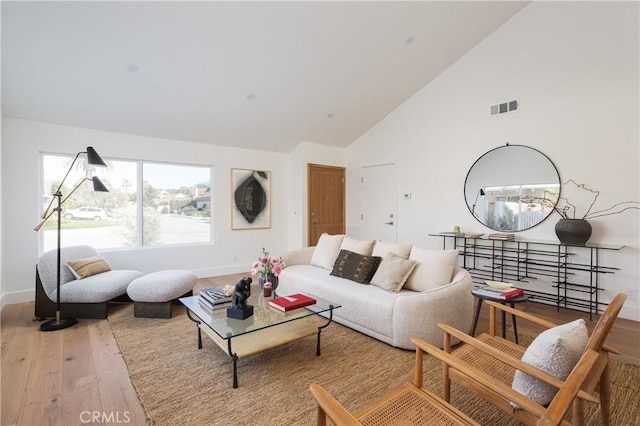 living room featuring high vaulted ceiling, visible vents, baseboards, and wood finished floors