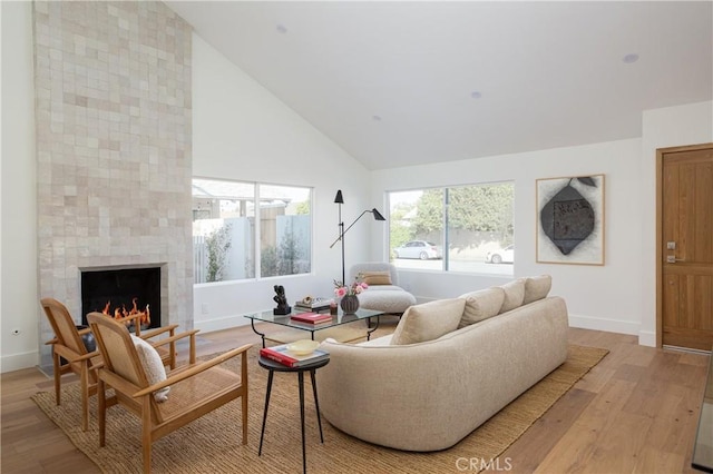 living room with baseboards, high vaulted ceiling, a fireplace, and light wood-style floors