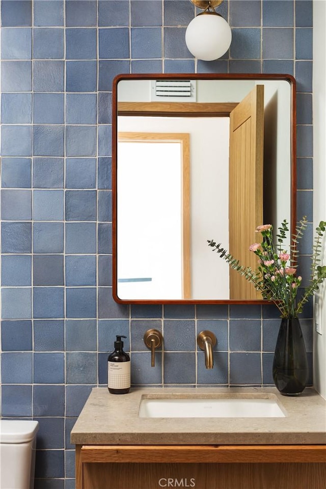 bathroom featuring toilet, backsplash, vanity, and tile walls