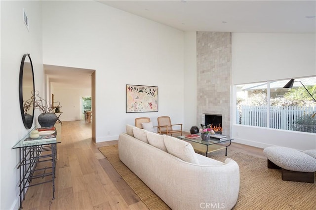 living area featuring high vaulted ceiling, plenty of natural light, a tiled fireplace, and wood finished floors