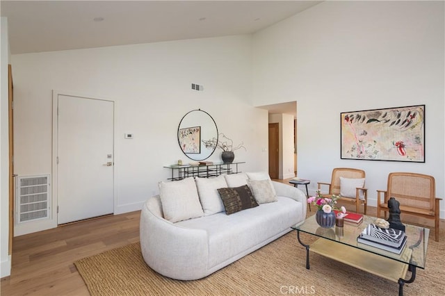 living room with light wood-style floors, baseboards, visible vents, and high vaulted ceiling