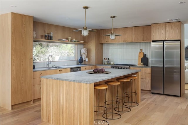 kitchen with appliances with stainless steel finishes, light wood-type flooring, a sink, and decorative backsplash