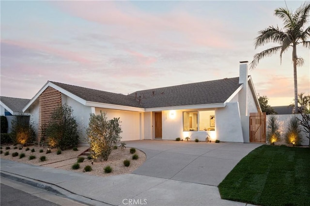 ranch-style house featuring a garage, a chimney, concrete driveway, and stucco siding