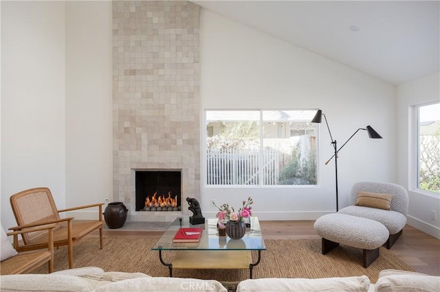 living room featuring high vaulted ceiling, a fireplace, baseboards, and wood finished floors