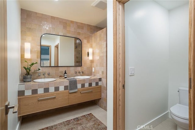 full bath featuring double vanity, a sink, toilet, and tile walls