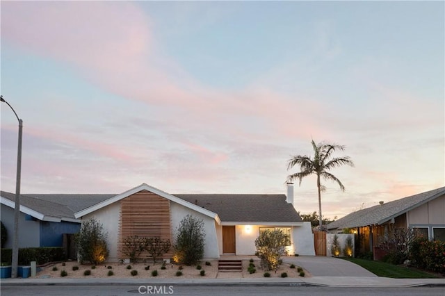 view of front facade with driveway, a chimney, and fence