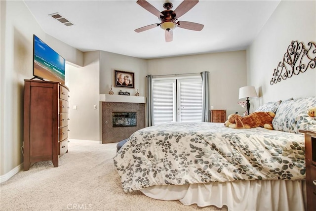 carpeted bedroom with baseboards, a glass covered fireplace, visible vents, and a ceiling fan