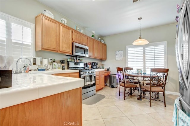 kitchen featuring decorative light fixtures, tile countertops, light tile patterned floors, stainless steel appliances, and a sink