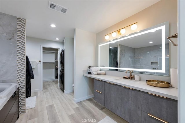 full bath featuring stacked washer / dryer, wood finished floors, vanity, visible vents, and a walk in closet