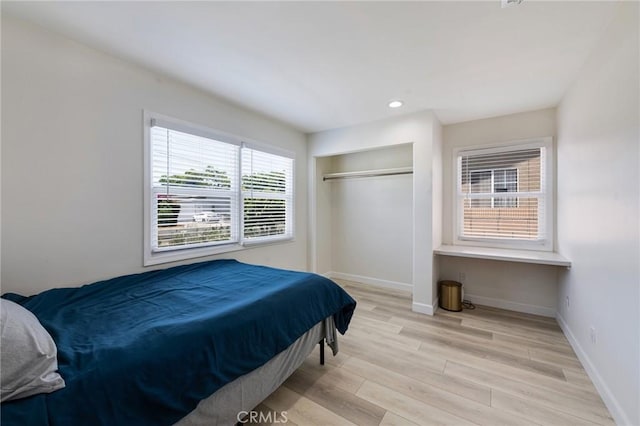 bedroom with built in desk, recessed lighting, a closet, light wood-style floors, and baseboards