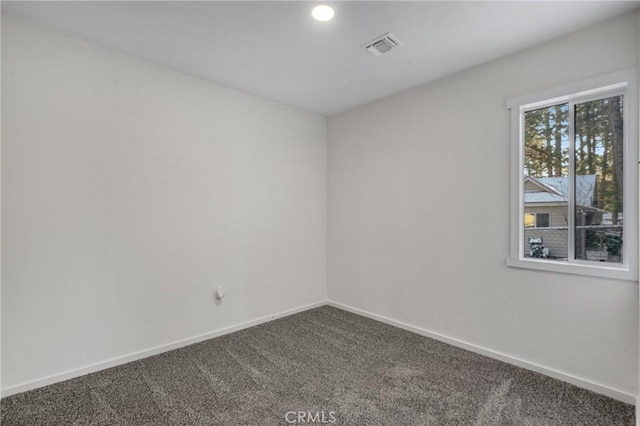 spare room with visible vents, dark carpet, and baseboards