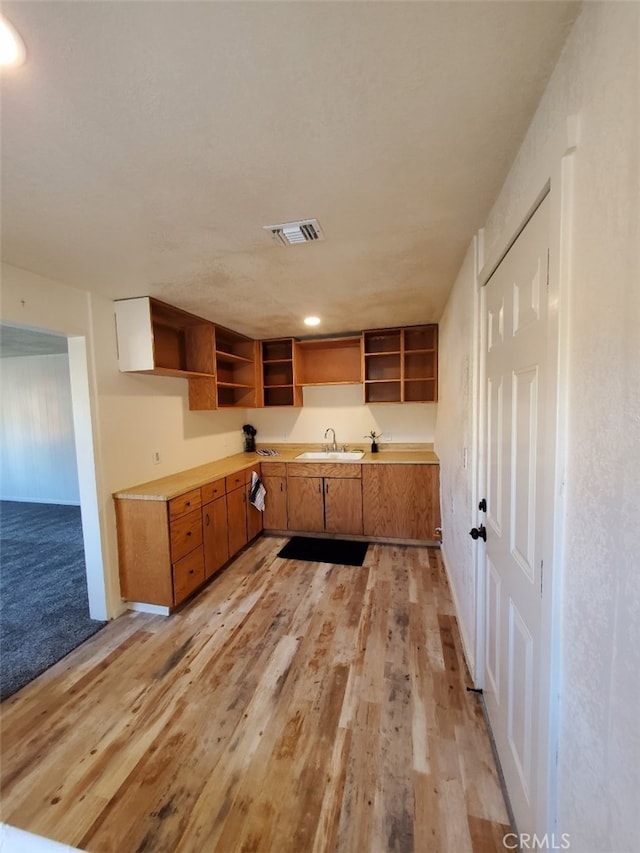 kitchen with light wood-type flooring, visible vents, open shelves, and a sink