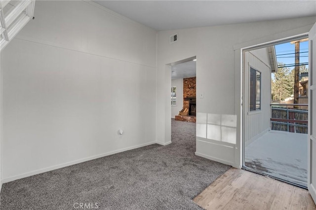 unfurnished room featuring lofted ceiling, carpet floors, visible vents, baseboards, and a brick fireplace