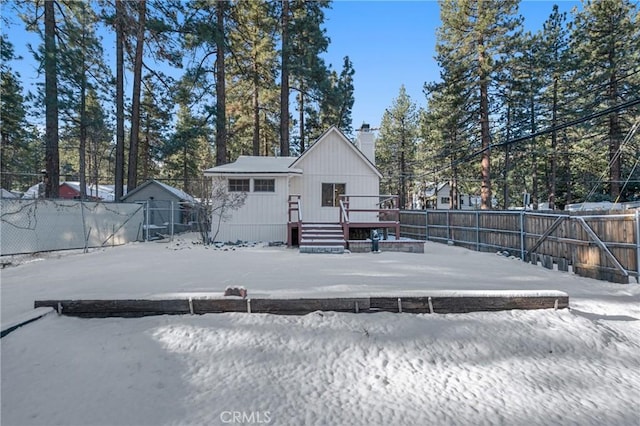 snow covered house with a chimney, a fenced backyard, and a deck