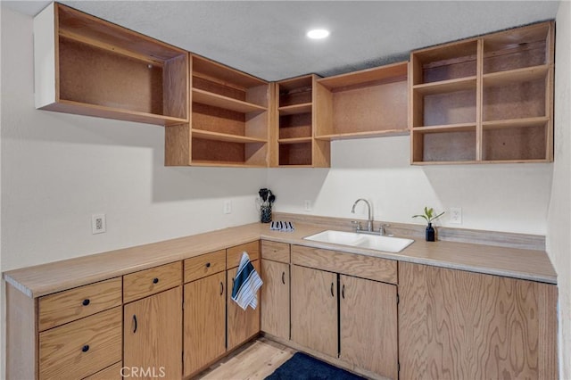 kitchen featuring open shelves, light wood finished floors, a sink, and light countertops