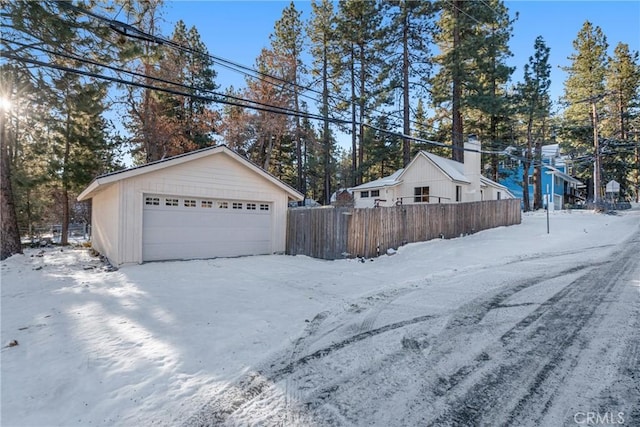 snowy yard featuring an outbuilding, a detached garage, and fence