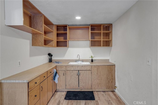 kitchen featuring open shelves, recessed lighting, light countertops, a sink, and light wood-type flooring