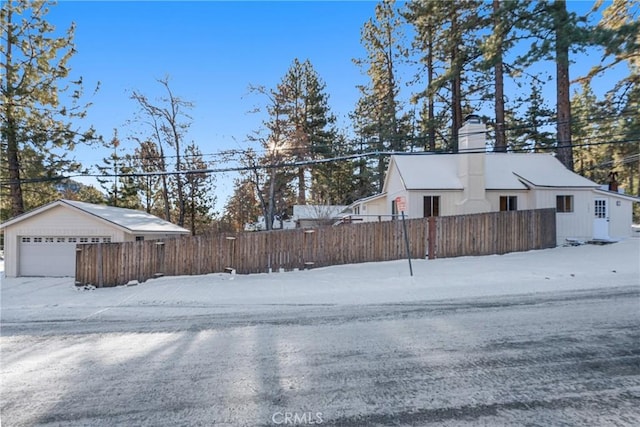 snowy yard with a fenced front yard, a detached garage, and an outbuilding