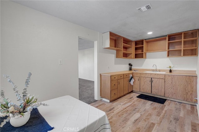 kitchen with open shelves, light wood-style flooring, a sink, and visible vents