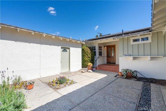 doorway to property featuring board and batten siding, stucco siding, and solar panels