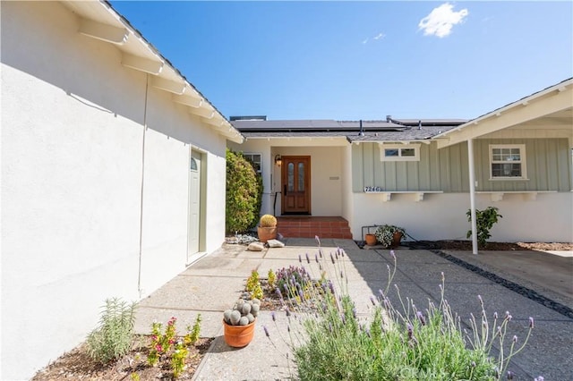 entrance to property featuring board and batten siding, stucco siding, and solar panels