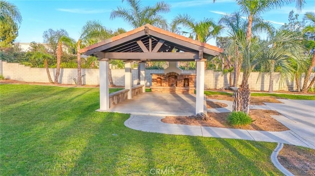 view of patio with an outdoor stone fireplace, fence, and a gazebo