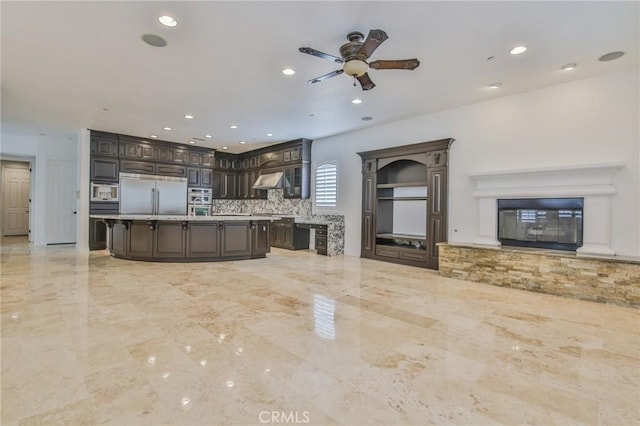 kitchen with stainless steel appliances, dark brown cabinets, light countertops, backsplash, and a glass covered fireplace