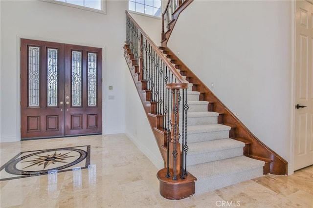 entrance foyer with a towering ceiling, marble finish floor, stairway, and baseboards